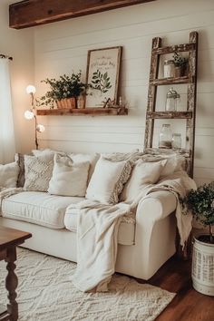 a living room with white couches, pillows and plants on the shelf above them