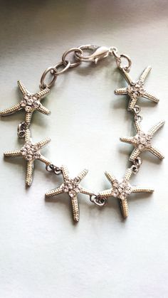 Most of our work revolves around the beach, sand, and sun. Have you ever held a starfish? They are super awesome and wiggle when held. We've always been fascinated by these wonderful sea creatures! Our bracelet features wonderful starfish about one inch in size with cute rhinestones in them. They really catch the light and would look great for your online meetings! We added extra links and a nice size lobster claw closure-cause we hate those tiny ones! This bracelet easily adjusts 7 to 8 inches Cheap Bracelets With Starfish Charm For Gift, Affordable White Charm Bracelet For Beach, Styx River, Sand Jewelry, White Wedding Favors, Bracelet Ocean, Starfish Jewelry, Starfish Bracelet, Tea Bag Holder