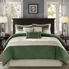 a bed with green and white comforters in a bedroom next to two lamps on either side of the bed