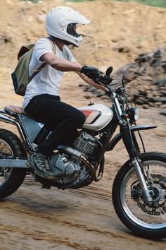 a man riding on the back of a white motorcycle down a dirt covered road,