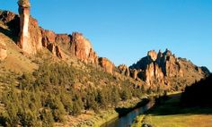 a river running through a lush green valley surrounded by tall rocks and trees in the distance