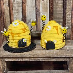 two cakes made to look like beehives on top of a wooden table with yellow decorations