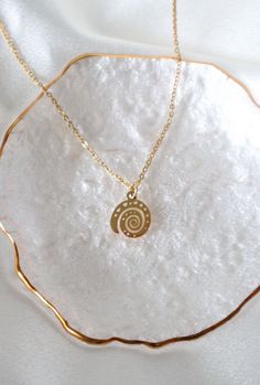 a gold necklace with a spiral design on it sitting on top of a white cloth