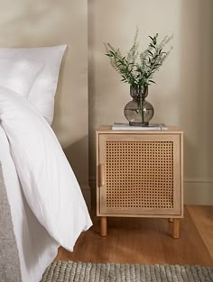 a bed with white sheets and pillows next to a night stand on a wooden floor