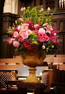 a large vase filled with lots of flowers on top of a wooden table next to chairs