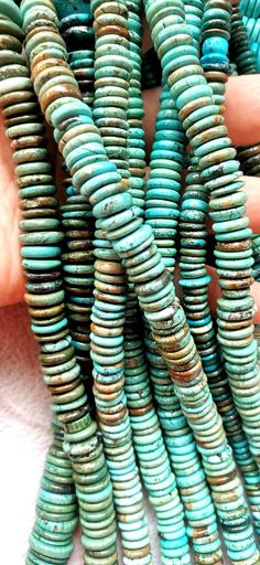 several turquoise beads are stacked together on a white surface and being held by someone's hand