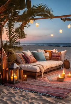 a couch sitting on top of a sandy beach next to the ocean with lit candles