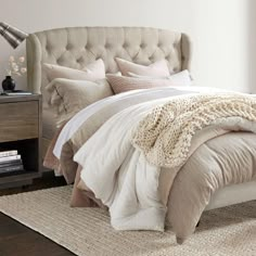 a bed with white sheets and pillows in a room next to a lamp on a table