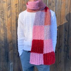 a woman wearing a pink, red and white scarf standing in front of a wooden fence