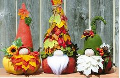 three decorative pumpkins with faces and leaves on them sitting in front of a fence