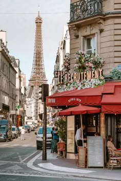 the eiffel tower is in the background of this street corner with people sitting at tables