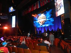 people are sitting in chairs and watching an event on the big screen at night time