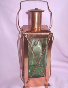 an old fashioned copper lantern with green glass in the front on a pink cloth background