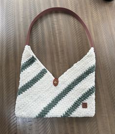 a white and green knitted purse sitting on top of a wooden table next to a pair of black shoes