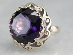 "A gorgeous purple amethyst with flashes of indigo and plenty of glitter is the centerpiece of this fabulous mid-century cocktail ring. A pierced scrolling scallop frame adds graphic interest and makes this piece unique to other ornate cocktail rings! Metal: 14K Yellow Gold Gem: Amethyst 17.69 Carats Gem Measurements: 17.2 mm, Round Ring Size: 6 Marks: \"14K\" Stamped on the inside band SKU #: N7UDRCEV Each piece has been identified and graded by a Graduate Gemologist who has been certified by t Yellow Gold Sapphire Ring, Amethyst Cocktail Ring, Right Hand Ring, Rings Metal, Vintage Cocktail Ring, Cameo Ring, Right Hand Rings, Hand Ring, Round Rings