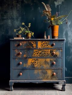 an old dresser with flowers and plants on it in front of a blue painted wall