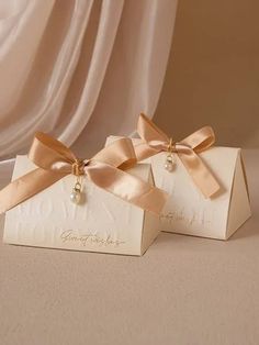 two white boxes with gold bows and pearls on them are sitting next to each other