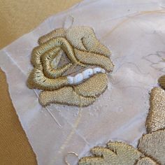 a piece of cloth with gold thread on it and a rose embroidered onto the fabric