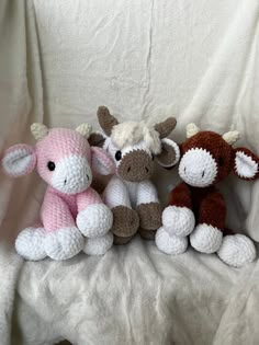 three crocheted stuffed animals sitting next to each other on a white cloth covered bed