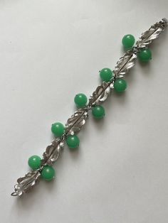 This is a stunning vintage silver tone metal and green Lucite bead cha-cha bracelet. The pieces signed Napier. It features a series of six dimensional leaf links with green beads in between the links. There are 10 beads This bracelet measures 8 inches long and is approximately 5/8 inches at the widest.  It appears to have never been worn. It is an excellent preowned vintage condition Vintage Green Round Bead Bracelets, Green Metal Beaded Bracelets For Jewelry Making, Vintage Green Beaded Bracelets, Vintage Green Round Beads Bracelet, Retro Green Bracelet Jewelry, Vintage Green Bracelets For Party, Green Metal Bracelets For Costume Jewelry, Green Metal Bracelet Costume Jewelry, Green Metal Bracelets For Formal Occasions