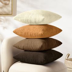 four pillows stacked on top of each other in front of a white chair with a basket