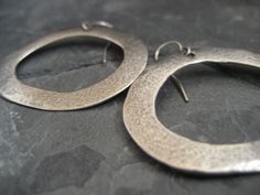 This item is made to order please allow 5 to 8 business days for your order to ship. A simple earring, yet with a lot of character. This is a great alternative to the classic round hoop. These whimsical hoop earrings where hand carved and cast .925 sterling silver. They have been lightly oxidized to reveal the uneven texture, which gives these earrings an organic feel. They measure 1 1/2 inches in width and 1 1/4 inches in height, and hang of a sterling silver ear wire. Minimalist Sterling Silver Oval Hoop Earrings, Classic Circular Sterling Silver Jewelry, Modern Rounded Sterling Silver Jewelry, Classic Sterling Silver Full Circle Jewelry, Unique Small Hoop Earrings For Everyday, Hand Forged Round Minimalist Earrings, Modern Small Hoop Earrings Hand Forged, Small Hoop Sterling Silver Earrings For Pierced Ears, Modern Silver Hoop Earrings With Sterling Clasp