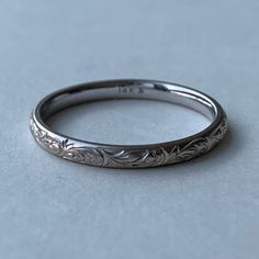 a wedding band with an engraved design on the outside and inside, sitting on a gray surface