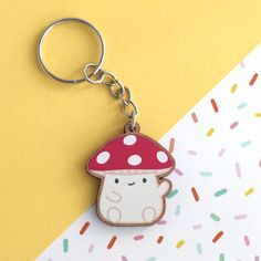 a mushroom shaped keychain with sprinkles around it on a yellow and white background