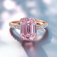 a pink diamond ring with diamonds around it on a white surface in front of a blurry background