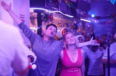 two people standing in front of a group of people at a party with their arms up