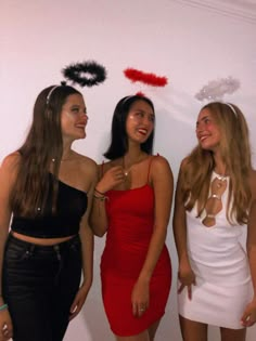 three beautiful young women standing next to each other in front of a white wall with red and black confetti on it