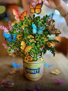 a person holding up a bouquet of flowers with butterflies flying around it on the table