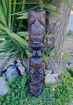 a tiki statue sitting next to a tree in front of some rocks and plants