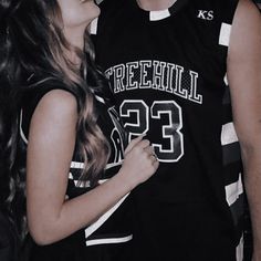 a man and woman standing next to each other in front of a basketball uniform on