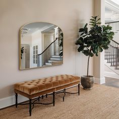 a living room with a bench, mirror and plant on the wall in front of it