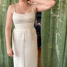 a woman in a white dress is brushing her hair and looking at the camera while standing next to a green curtain