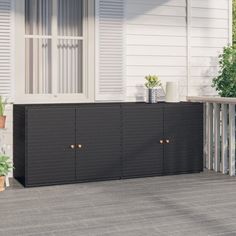 a black cabinet sitting on top of a wooden deck next to a white house with shutters