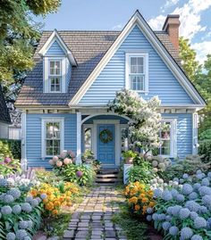 a blue house surrounded by flowers and greenery in the front yard with a pathway leading to it