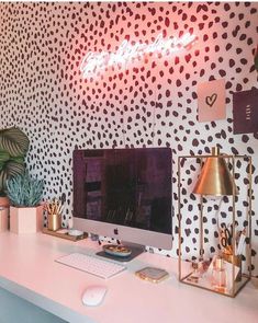 a desk with a computer on top of it next to a potted plant and a neon sign