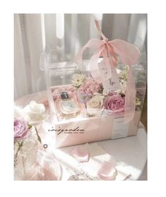 a pink box with flowers and perfume bottles in it sitting on a table next to a window