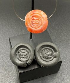 two wax seals with faces on them sitting on a black stand next to an orange object