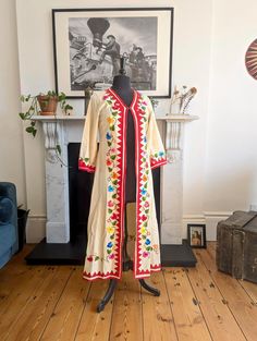 Discover a piece of history with this exquisite Vintage 1970's Mexican Hand Embroidered Linen Jacket Robe. Unique and timeless, this robe is a testament to the intricate craftsmanship and vibrant style of the 70's era Era: 1970's Material: high-quality linen Design: Hand embroidered floral patterns on the front, hem, and cuffs Closure: Single eyelet at the top Size: Small (UK 8) Pit to pit 41cm Sleeve length 46cm Shoulder Width 36cm Full length 120cm Waist 46cm Condition: excellent vintage condi Vintage Long Sleeve Kimono For Festival, Vintage Long Sleeve Robe For Spring, Vintage Long Sleeve Kaftan For Spring, Festive Vintage Embroidered Kaftan, Vintage Long Sleeve Kimono For Festive Occasions, Vintage Long Sleeve Kaftan For Festival, Cream Long Sleeve Embroidered Kaftan, Vintage Long Embroidered Outerwear, Vintage Long Fitted Robe