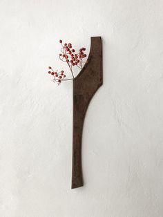 a piece of metal with some red flowers on it's end and a white wall in the background