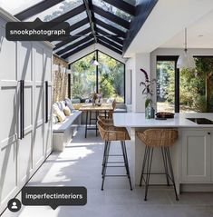 an open kitchen and dining area with white cabinets, counter tops and bar stools