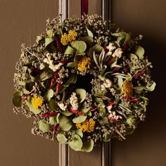 a wreath hanging on the front door of a house decorated with flowers and greenery