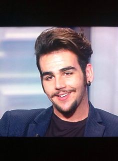 a man is smiling while sitting in front of a tv screen with his hair pulled back