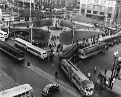 an old black and white photo of buses on the street with people standing around them