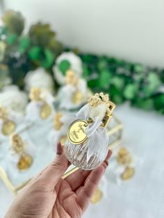 a hand holding a small glass bottle with gold trimmings on it and some other items in the background