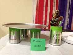 a table with tin cans and a sign that says mutant slime on it next to a cake stand