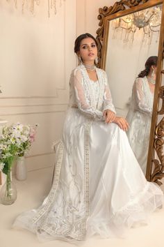 a woman sitting in front of a mirror wearing a white dress with beading on it